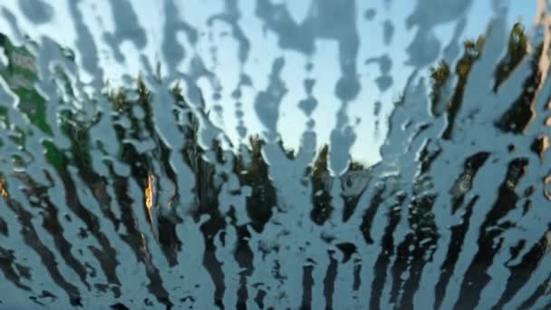 青と赤の光に照らされた自動屋外洗車場で車のフロントガラスに流れる泡の手持ちカメラショット 他の車が通過見ます — ストック動画