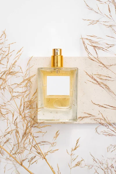 Beyaz arka planda taş tabakta saydam bir parfüm şişesi. Gün ışığıyla parfüm sunumu.