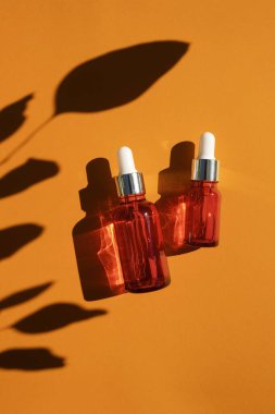 Turuncu arka planda gümüş kapaklı kırmızı cam damlalar. Güzel gün ışığında cilt bakımı ürünleri.