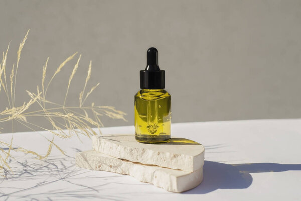 Бутылка зеленого стекла с черной крышкой на подиуме с сухими растениями на светлом фоне.