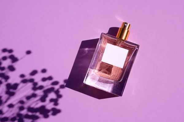 Transparent flaska parfym på en lila bakgrund. Doftpresentation med dagsljus. — Stockfoto