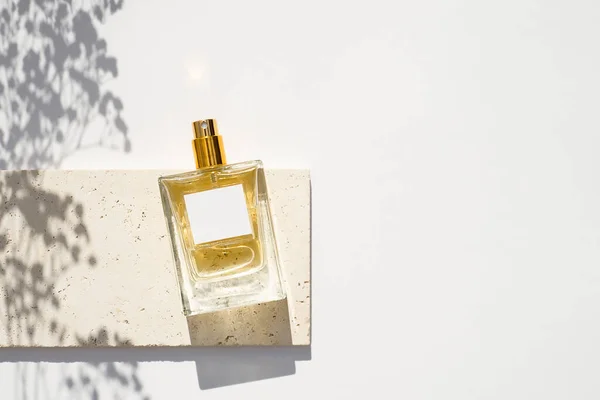 Transparante fles parfum met wit etiket op stenen plaat op een witte achtergrond. — Stockfoto