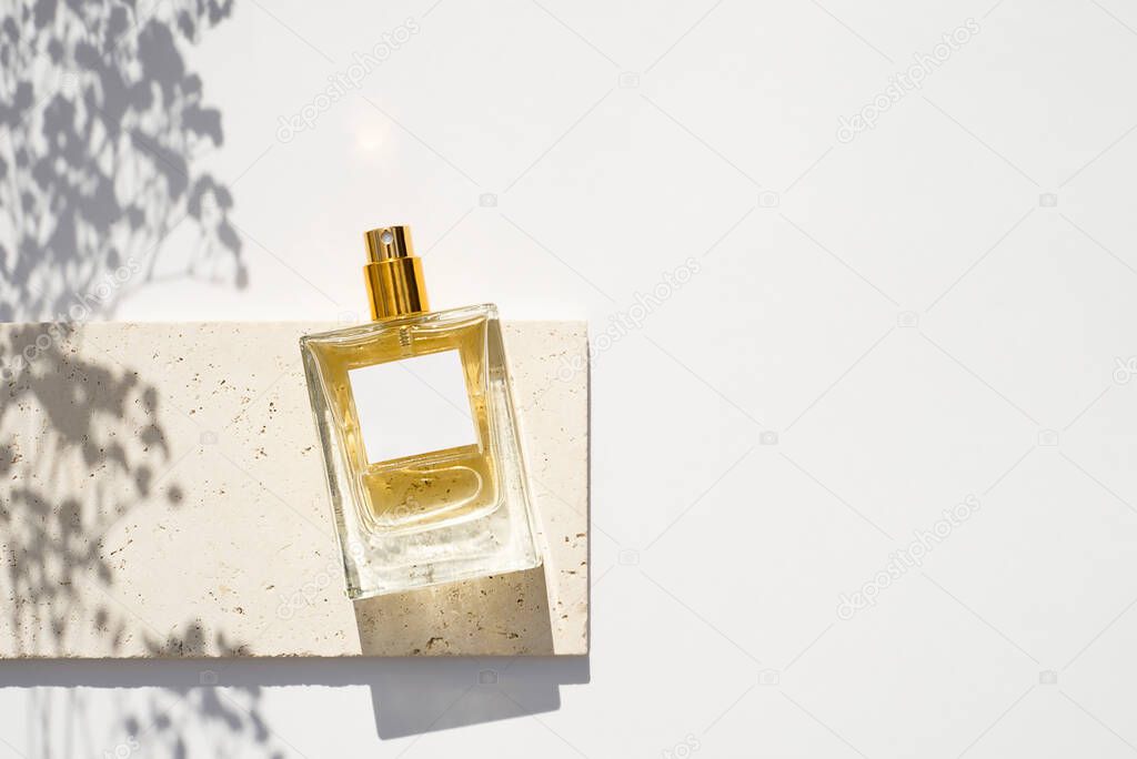Transparent bottle of perfume with white label on stone plate on a white background.