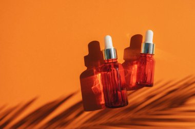 Turuncu arka planda gümüş kapaklı kırmızı cam damlalar. Güzel gün ışığında cilt bakımı ürünleri.
