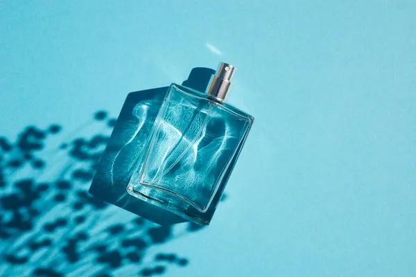 Frasco transparente de perfume sobre fondo azul. Presentación de fragancias con luz natural —  Fotos de Stock
