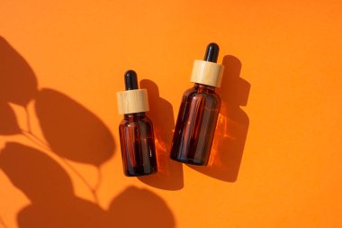 Kehribar cam damlaları farklı boyutlarda, turuncu arka planda bambu kapaklı. Bitki gölgesi olan üst görünüm.