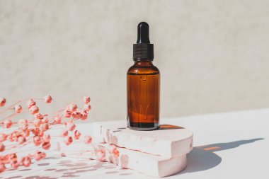 Podyumda siyah kapaklı kehribar cam damlası şişesi ve arka planda kuru bitkiler. Cilt bakım ürünleri, doğal kozmetik ürünleri. Yüz ve vücut bakımı için güzellik konsepti