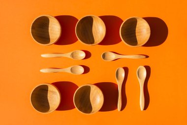 Kaşıklı boş ahşap kaseler. Turuncu arkaplanda en üstte duran tabak takımları.