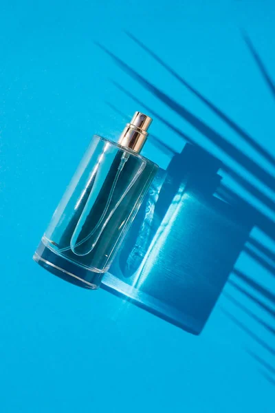 Przezroczysta butelka perfum na niebieskim tle. Prezentacja zapachu przy świetle dziennym. T — Zdjęcie stockowe