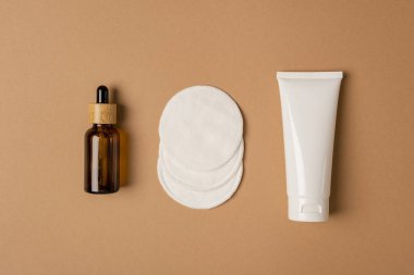 Krem ya da losyon için plastik beyaz tüp ve yeniden kullanılabilir pamuk mermileri, bej arka planda kehribar cam damlası şişesi.