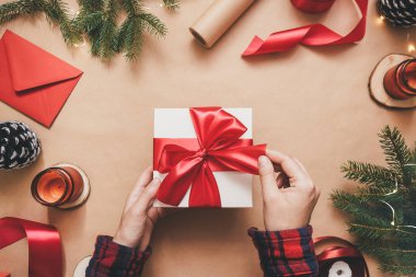 Kırmızı kurdeleli beyaz hediye kutusu Kraft arka planında el ele tutuşuyor..