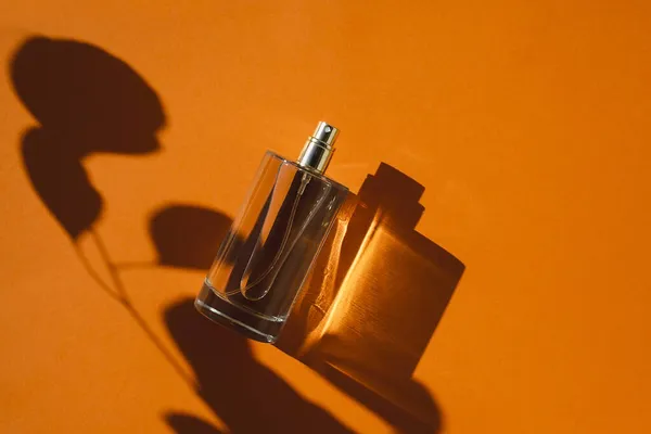 Átlátszó parfümös üveg narancssárga háttérrel. Illatanyag-kiszerelés nappal. — Stock Fotó