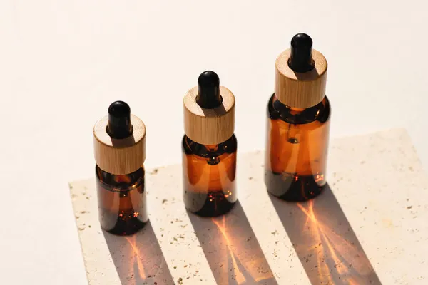 Bouteilles compte-gouttes en verre ambré avec couvercle en bambou sur plaque de pierre. Produits pour la peau, cosmétiques naturels — Photo