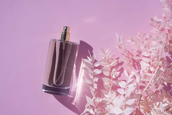 Transparente Flasche Parfüm auf rosa fliederfarbenem Hintergrund. Duftpräsentation mit Tageslicht. — Stockfoto