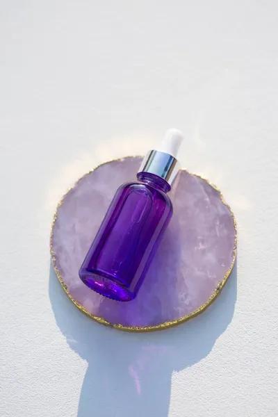 Pódio de pedra conta-gotas de vidro roxo no fundo branco. Produtos para a pele, cosméticos naturais. — Fotografia de Stock