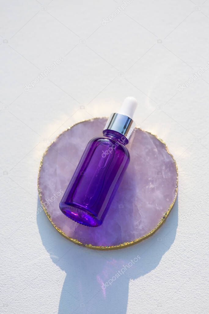 Purple glass dropper bottle stone podium on white background. Skincare products, natural cosmetic.