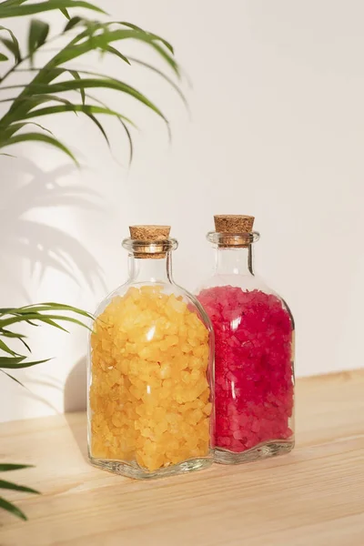 Dos botellas transparentes llenas de sal marina amarilla y roja sobre fondo de madera natural. — Foto de Stock