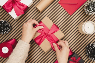 Çizgili arka planda el işi hediye paketi yapan genç bir kadın..