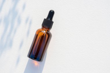 Siyah kapaklı kehribar cam damlası şişesi. Beyaz arkaplanda bitki gölgesi olan üst görünüm. Cilt kozmetiği. Yüz bakımı için güzellik konsepti