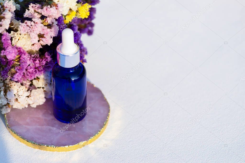 Blue glass dropper bottle on white background with dry flowers. Container mockup with cosmetic oil or serum. Showcase for the presentation skincare products.