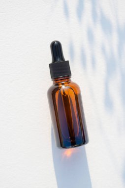 Siyah kapaklı kehribar cam damlası şişesi. Bitki gölgesi ile beyaz arkaplanda üst görünüm.