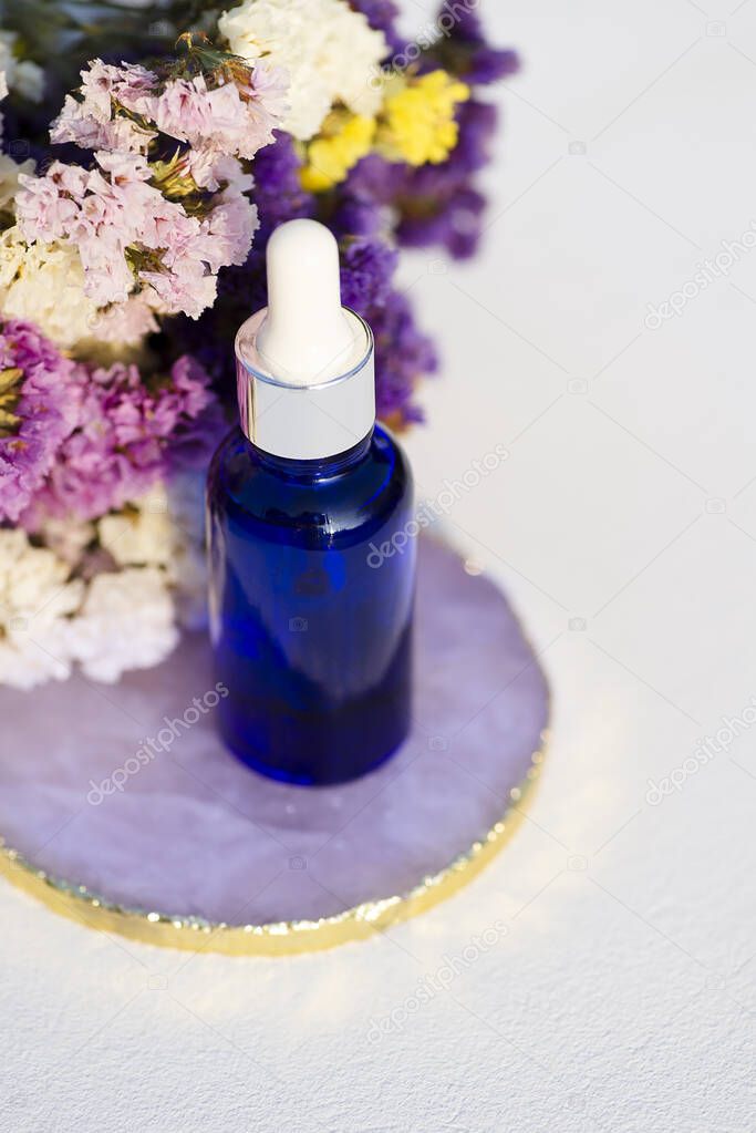Blue glass dropper bottle on white background with dry flowers.