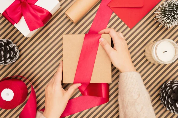 Giovane donna che fa arco per scatola regalo artigianale su sfondo a strisce. — Foto Stock