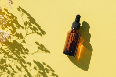 Siyah kapaklı kehribar cam damlası şişesi. Sarı arkaplanda bitki gölgesi olan üst manzara. Cilt kozmetiği. Yüz bakımı için güzellik konsepti