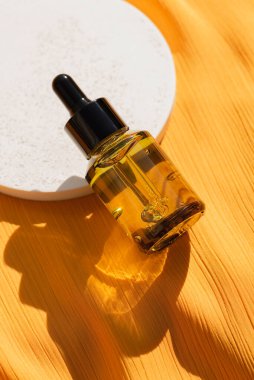 Sarı kumaş arka planında beyaz kürsüde pipeti olan yeşil cam damlacık şişesi. Konteynırda kabarcıklar olan jel dokusu. Cilt bakım ürünleri, doğal kozmetik ürünleri. Yüz ve vücut bakımı için güzellik konsepti.