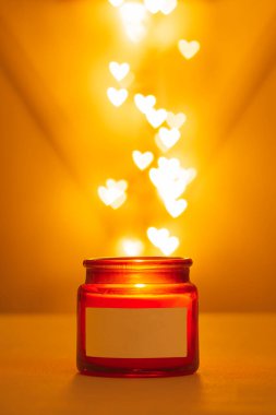 Cam, kırmızı, kahverengi kavanoz. Arka planda yanan bir mum. Kupa şeklinde bokeh ışıkları. Aromalı ev konforu. Yazı için etiket.