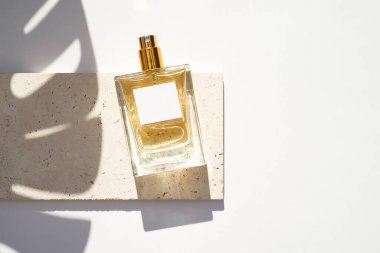 Beyaz arka planda beyaz etiketli saydam bir parfüm şişesi. Gün ışığıyla güzel kokulu bir sunum. Palmiye yaprağı gölgeli doğal malzemelerde moda kavramı.