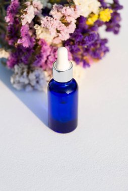 Beyaz arka planda mavi cam damlalar ve kuru çiçekler. Kozmetik yağlı ya da serumlu konteynır modeli. Sunum için sunum cilt ürünleri.