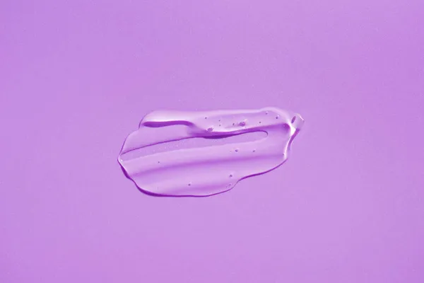 Cosmetic smear. Appearance of the texture of the transparent gel on purple background. — Stock Photo, Image