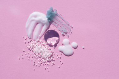 Kozmetik lekeler ve damlalar. Pembe arka planda krem, yağ ve granüllerin dokusunun görünümü. Doğal cilt bakım ürünleri. Yüz ve vücut bakımı için güzellik konsepti