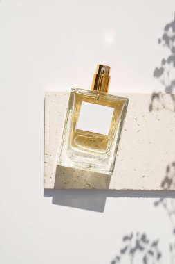 Beyaz arka planda beyaz etiketli saydam bir parfüm şişesi. Gün ışığıyla güzel kokulu bir sunum. Kuru bitki ile doğal maddelerin moda konsepti. Kadın ve erkeğin özü..