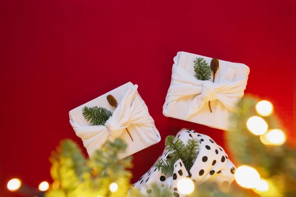 Ökologische und nachhaltige Geschenkideen. Weiße Geschenkschachtel aus Stoff auf rotem Hintergrund. Furoshiki-Wrap und Bokeh-Lichter. — Stockfoto