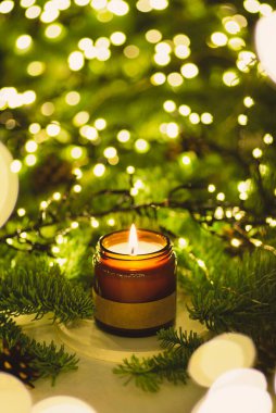 Kavanozdaki mumlar, yeşil Noel ağacı dalları ve ışıklarının arka planında. Aromalı ev konforu. Şölen için dekor arkaplanı. Güzel doğal bokeh.