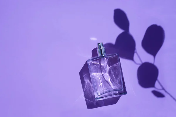 Frasco transparente de perfume sobre fondo púrpura. Presentación de fragancias con luz natural —  Fotos de Stock