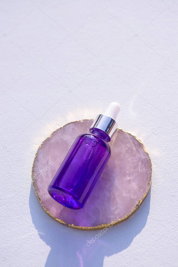 Purple glass dropper bottle stone podium on white background. Skincare products, natural cosmetic. Beauty concept for face and body care.