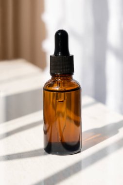 Siyah kapaklı kehribar cam damlası şişesi. Doğal güneş ve gölgeler. Gündüz vakti beyaz arka plan. Cilt bakım ürünleri, doğal kozmetik ürünleri. Yüz ve vücut bakımı için güzellik konsepti