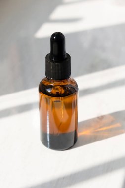 Siyah kapaklı kehribar cam damlası şişesi. Doğal güneş ve gölgeler. Gündüz vakti beyaz arka plan. Cilt bakım ürünleri, doğal kozmetik ürünleri. Yüz ve vücut bakımı için güzellik konsepti
