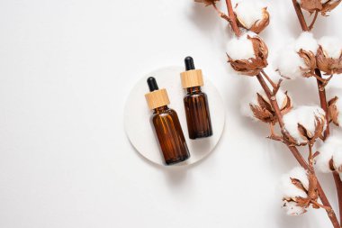 Bambu kapaklı Amber cam damlaları ve beyaz beton kürsüde pamuk çiçekleri. Cilt kozmetiği. Yüz bakımı için güzellik konsepti. Gün ışığıyla sunum.