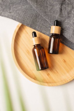 Ürün sunumu için ahşap tabakta bambu kapaklı Amber cam damlası şişeleri. Gri kumaşta cilt kozmetiği. Yüz bakımı için güzellik konsepti
