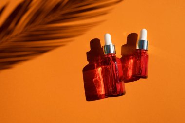 Turuncu arka planda gümüş kapaklı kırmızı cam damlalar. Güzel gün ışığında cilt bakım ürünleri. Doğal bitki gölgesi ile doğal kozmetik konsepti. Yüz ve vücut bakımı için güzellik kavramı.