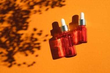 Turuncu arka planda gümüş kapaklı kırmızı cam damlalar. Güzel gün ışığında cilt bakım ürünleri. Doğal bitki gölgesi ile doğal kozmetik konsepti. Yüz ve vücut bakımı için güzellik kavramı.