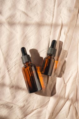 Kehribar cam şişelerde damla pipeti serumla ya da açık gri kumaş arka planında gerekli yağla. Cilt bakımı kozmetik sunumu. Gün ışığı ve gölge bırakır. Yüz bakımı için güzellik konsepti