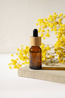 Kehribar cam şişe ve damlatan pipetle serum ya da ürün sunumu için beton tabakta gerekli yağ. Sarı kuru bitkilerle cilt kozmetiği. Yüz bakımı için güzellik konsepti