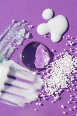 Kozmetik lekeler ve damlalar. Mor arka planda krem, yağ ve granüllerin dokusunun görünümü. Doğal cilt bakım ürünleri. Yüz ve vücut bakımı için güzellik konsepti