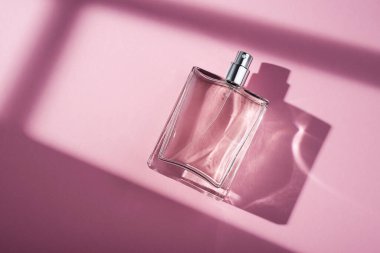 Pembe arka planda saydam bir parfüm şişesi. Gün ışığıyla güzel kokulu bir sunum. Pencere gölgesi olan doğal malzemelerde moda bir kavram. Kadın özü..