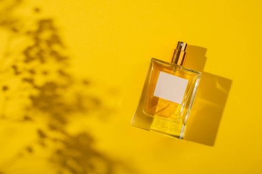 Sarı arka planda etiketi olan saydam bir parfüm şişesi. Gün ışığıyla güzel kokulu bir sunum. Pencere gölgesi olan doğal malzemelerde moda bir kavram. Kadın özü..